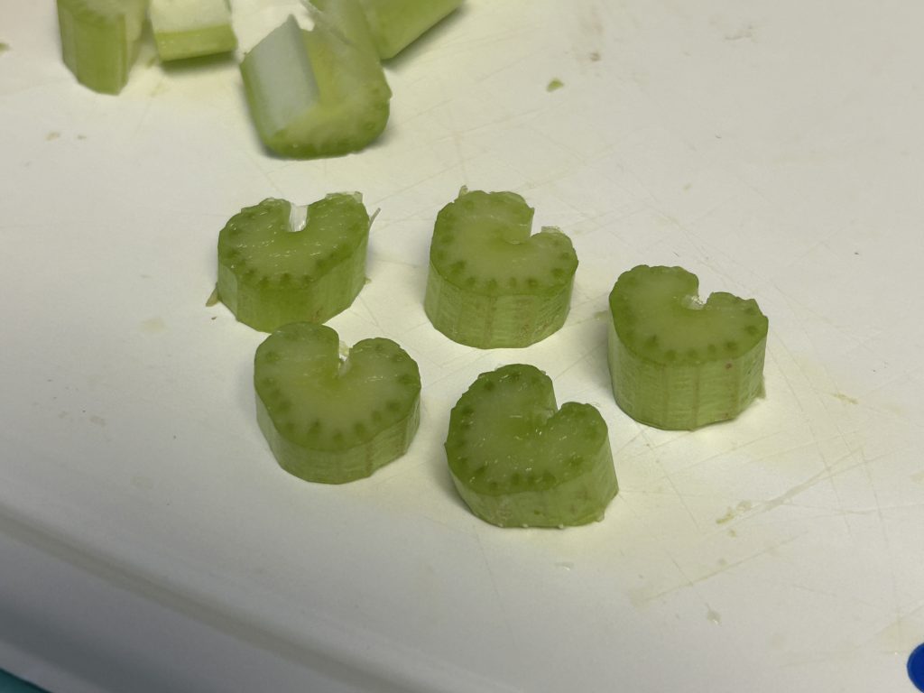 Picture of five pieces of celery shaped like hearts laying on a cutting board.